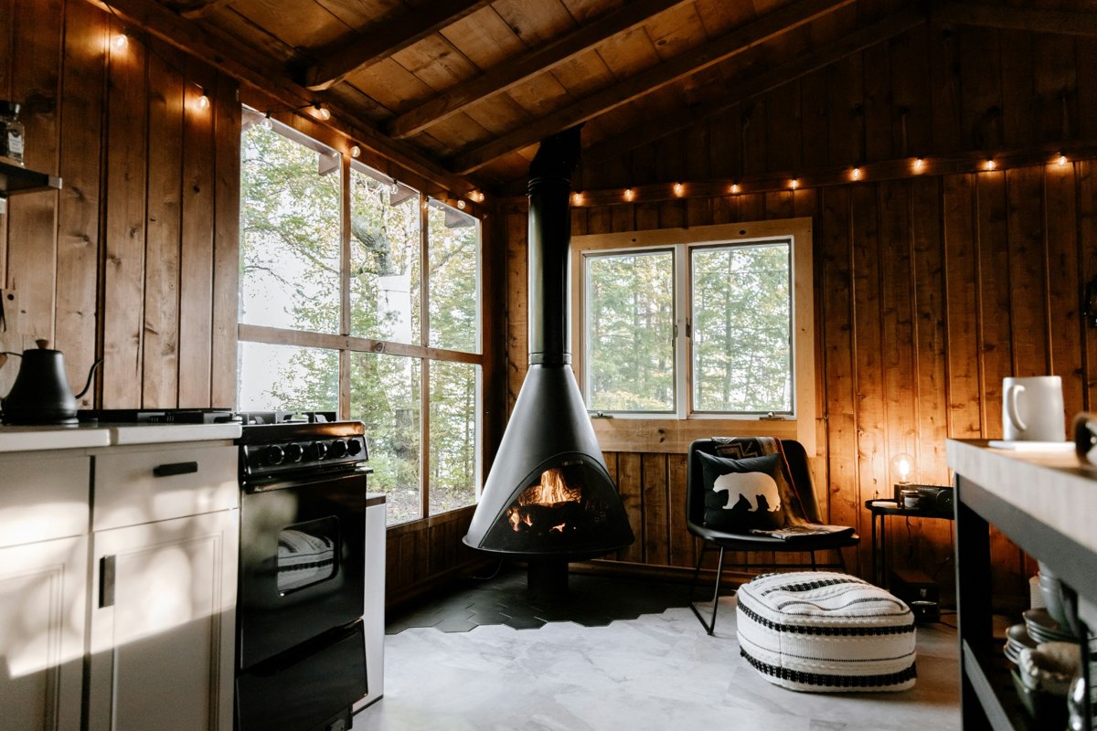 A cosy wood-lined cabin with a fireplace and forest views