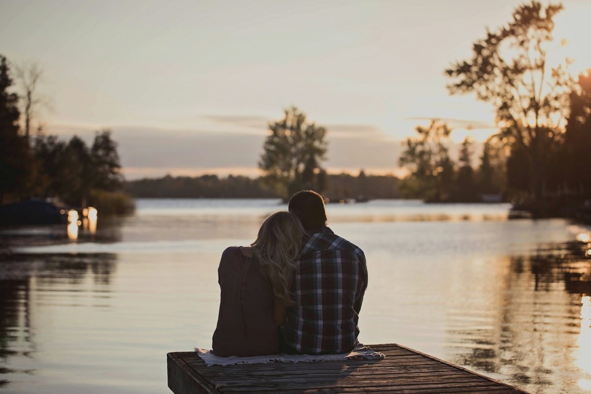 Two people sitting together on a dock beside a quiet lake
