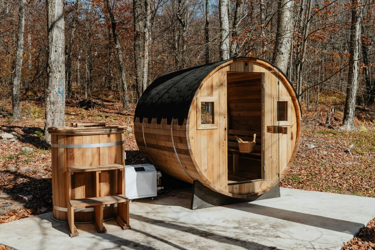 A wooden barrel sauna and outdoor tub among the trees