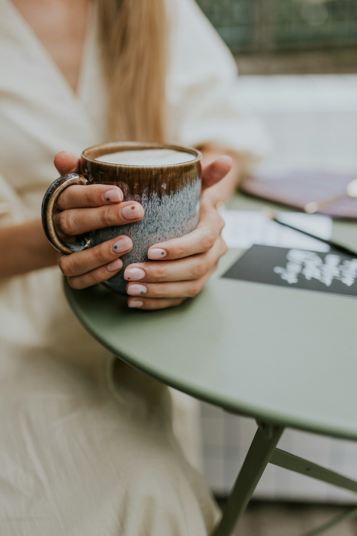 Hands wrapped around a ceramic coffee cup at an outdoor table